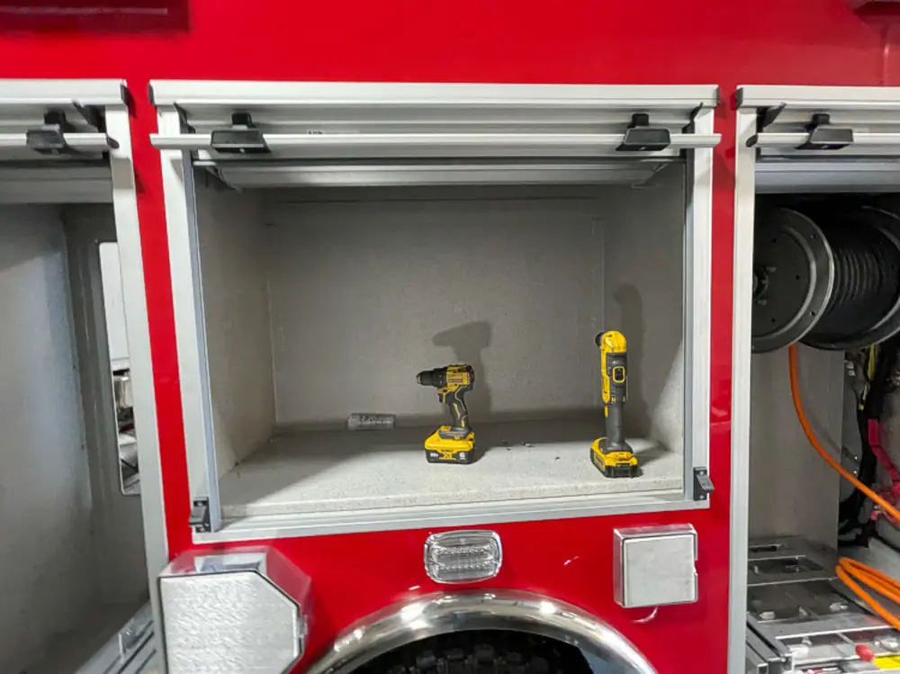 Exterior view of small fire truck showing cab, body compartments, and wheel/tire area.